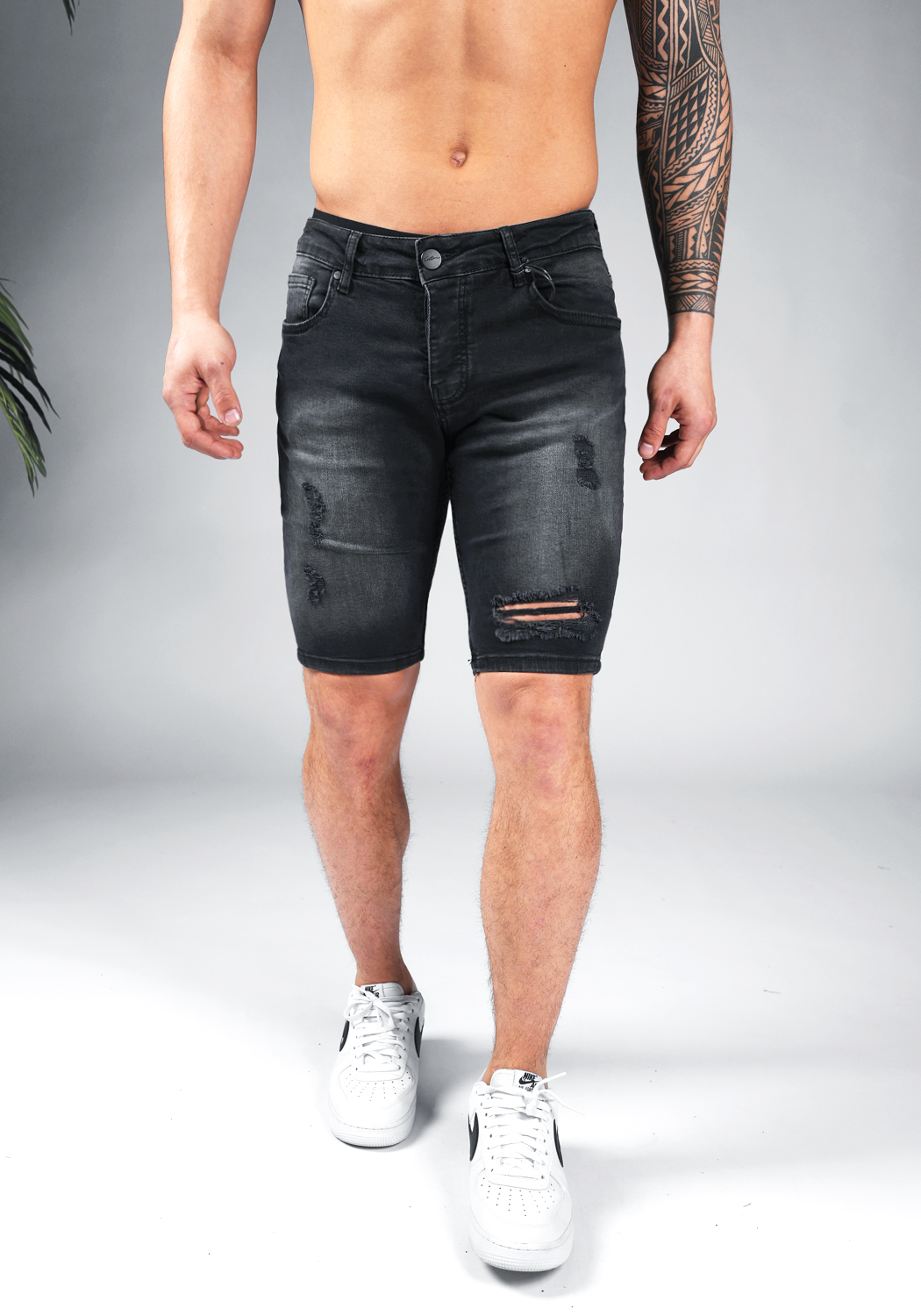 chark shorts 2023 2a Vooraanzicht van model gekleed in zwarte jean shorts met damaged details in combinatie met witte sneakers.