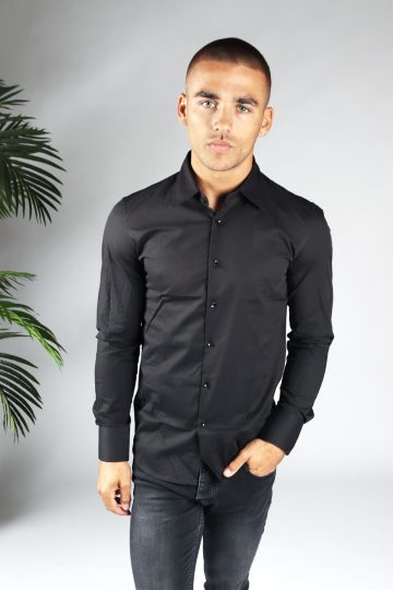 Vooraanzicht van heren overhemd in een zwarte kleur, met zwarte knoopjes en een slimfit pasvorm. Het model draagt een donkere jeans en heeft zijn linkerhand in zijn linker broekzak.